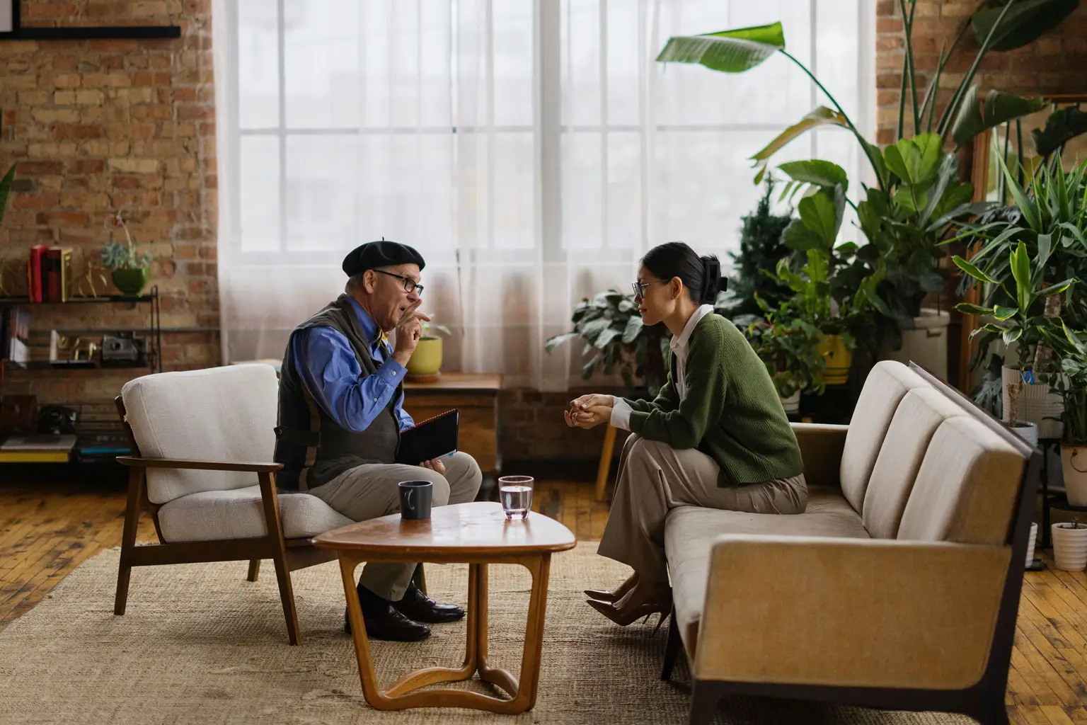 A therapist and a client talking in a bright, plant-filled room.